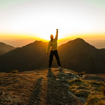 bible verses about hard work person standing on top of mountain at sunset with fist in the air