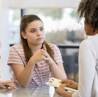 serious mom talks with her daughters high school counselor the teenage girl is sitting next to her mom with a blank expression on her face