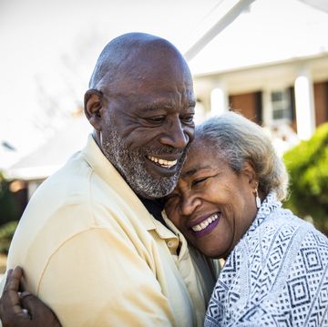 senior couple embracing in front of residential home