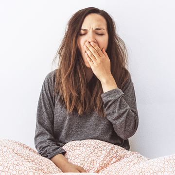 girl under bedsheets yawning from fatigue